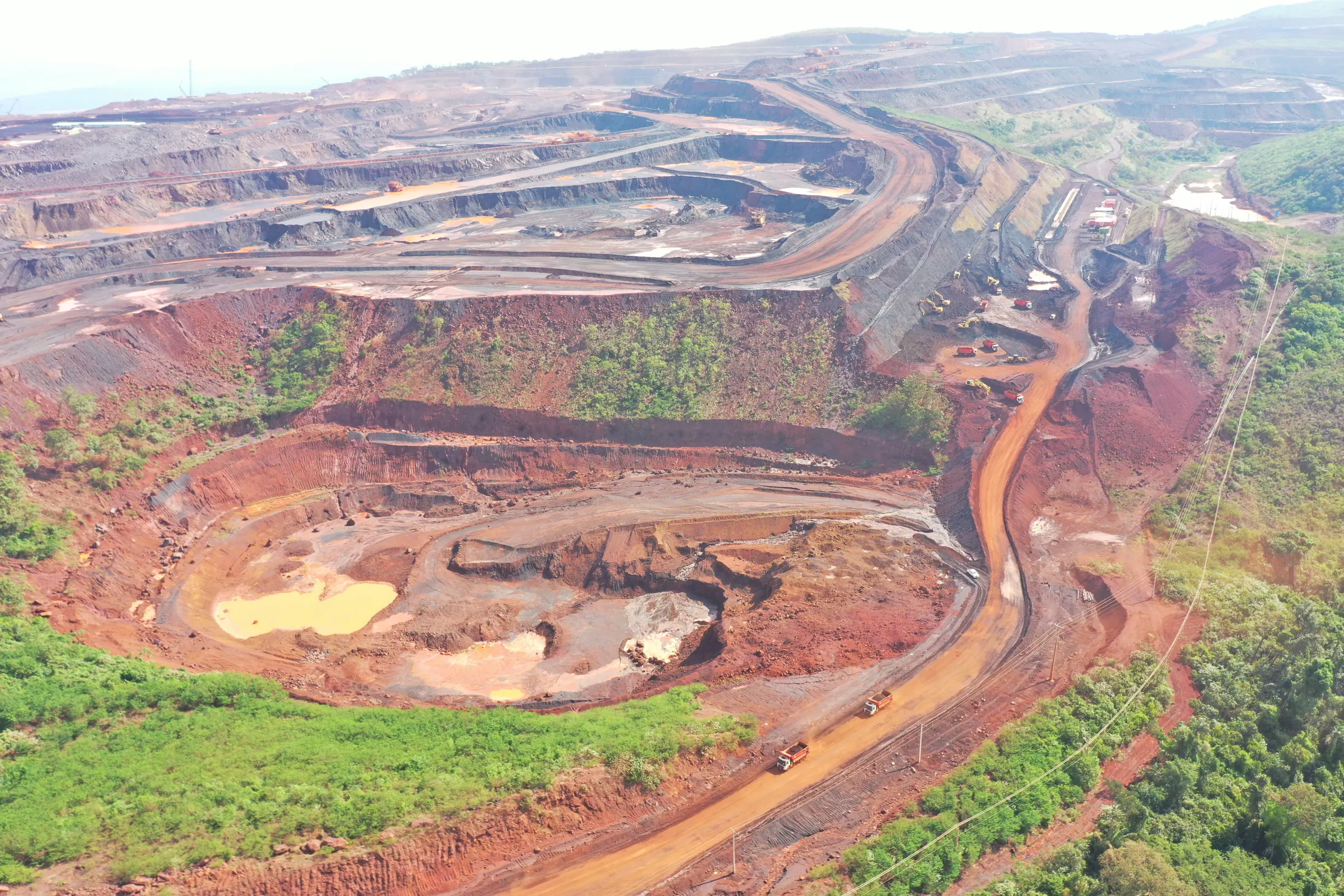 Vista aérea de cava de mina a céu aberto, com bancadas, estradas de serviço e mata ao redor